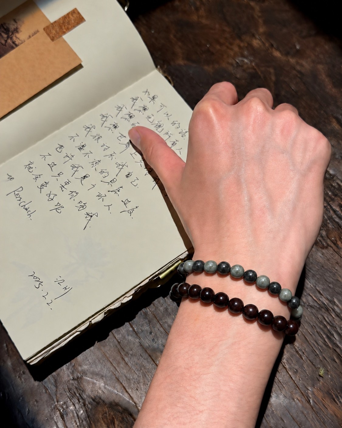A hand writing in a notebook, two strands of beads on the wrist (No. 04)