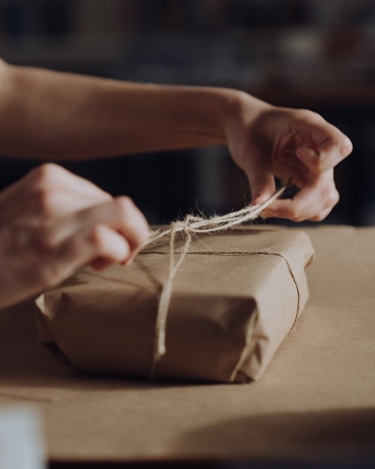 Two hands pull a cord tight around a small parcel wrapped in plain paper
