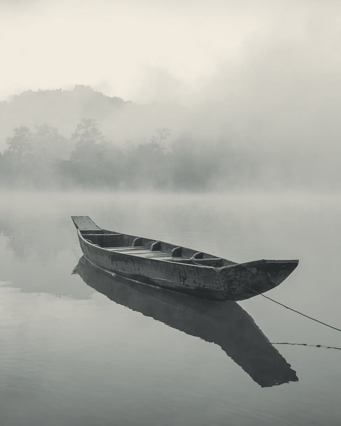 A long wooden boat tied up on still, misty water